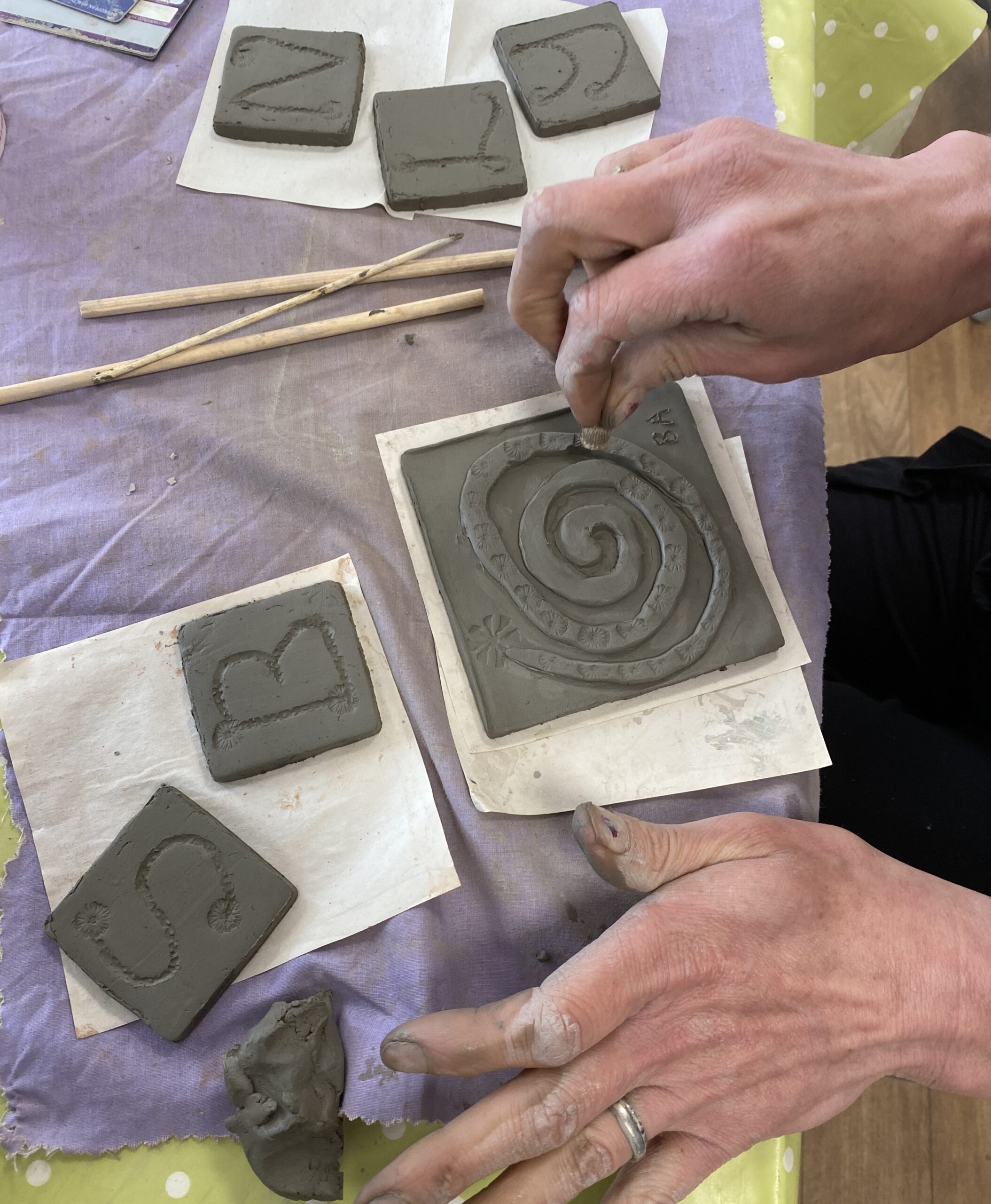 Hands making a clay tile and patterning the tile